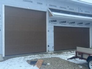 Two brown garage doors installed on a house under construction, showcasing work by McDonald Overhead Door Inc. in Kenosha, WI.