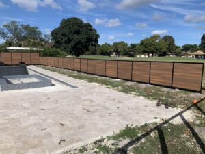 A brown horizontal slat fence with black posts installed next to a pool area by Miami Fence Installation Contractors in Miami, FL.