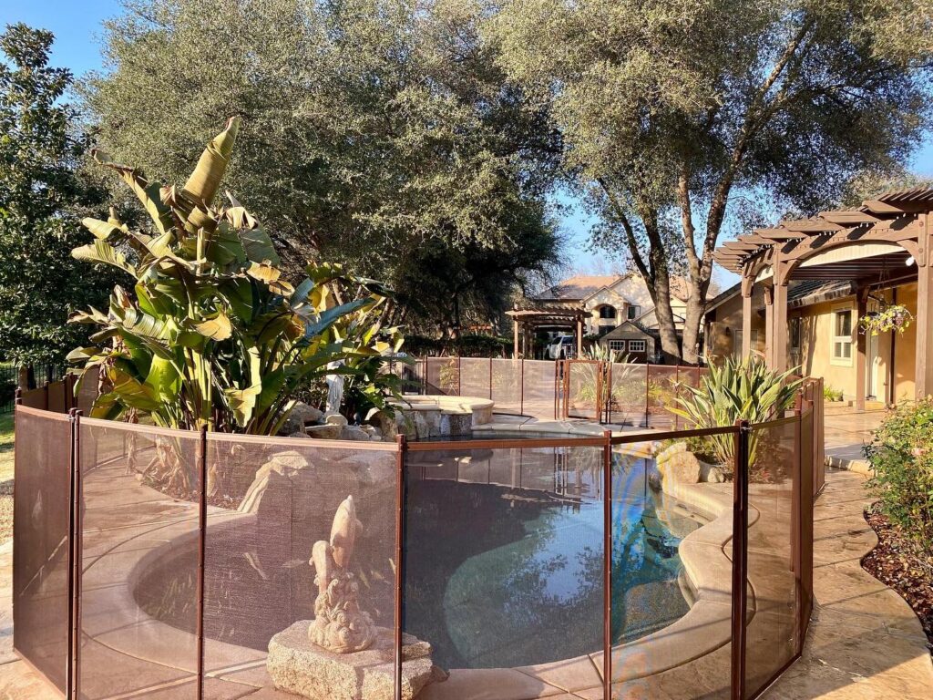 A brown mesh pool fence installed around a backyard pool, offering safety from Golden State Baby Barrier in Sacramento, CA.
