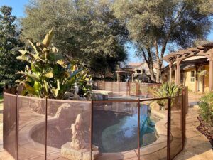 A brown mesh pool fence installed around a backyard pool, offering safety from Golden State Baby Barrier in Sacramento, CA.