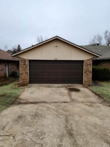 A brown residential garage door installed on a brick house by Entry Garage Door in Shawnee, OK.