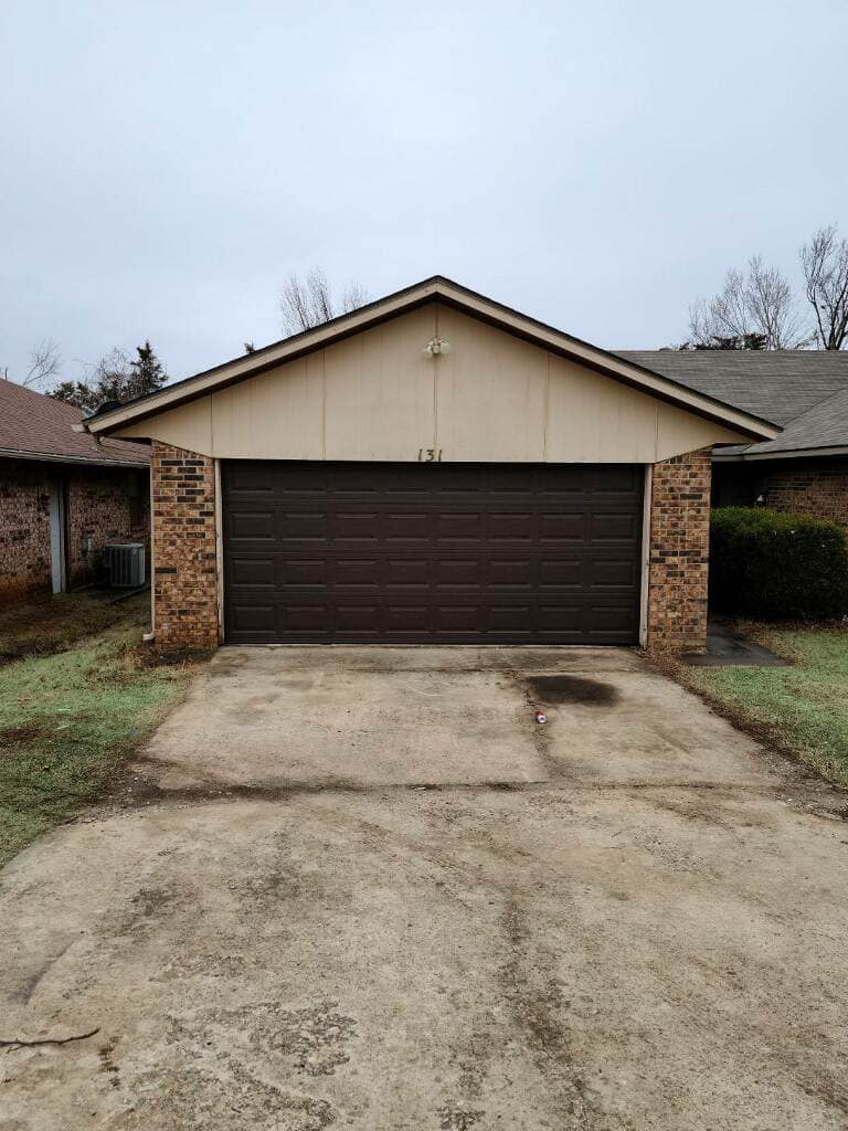 A brown residential garage door installed on a brick house by Entry Garage Door in Shawnee, OK.