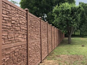 A long, brown textured privacy fence, possibly composite or faux stone, installed by RUCO Fence in Huntsville, AL.