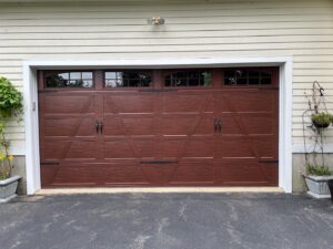 A brown wood-grain garage door with decorative hardware and windows installed by PM Garage Door in Hudson, NH.