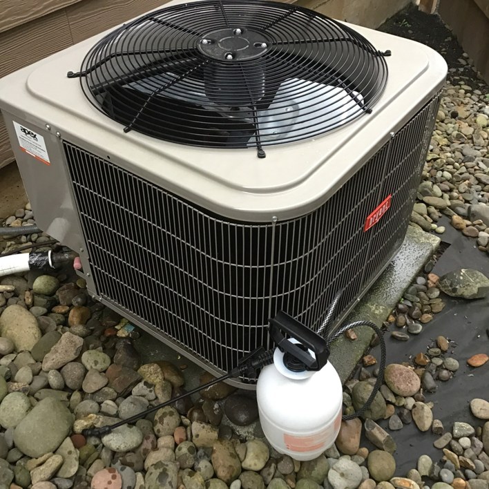 A Bryant outdoor HVAC condenser unit being cleaned or maintained with a sprayer bottle by KAP'S HVAC in Portland, OR.