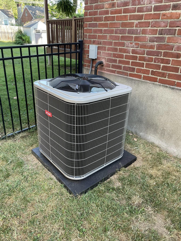 A Bryant HVAC condenser unit installed outdoors next to a brick wall and fence by Bowmans Heating and Air LLC in Middletown, KY