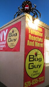 The exterior of Bug Guy Pest Control building at night, advertising bed bug, termite, and roach services in Las Cruces, NM.