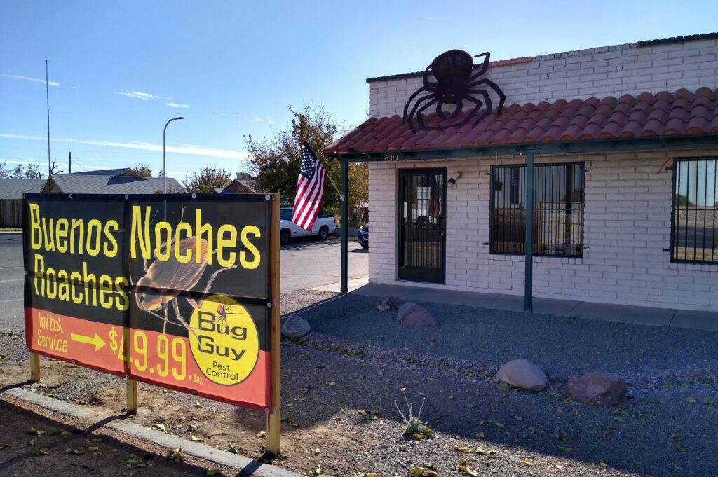 The exterior of Bug Guy Pest Control building with a 'Buenos Noches Roaches' sign in Las Cruces, NM.