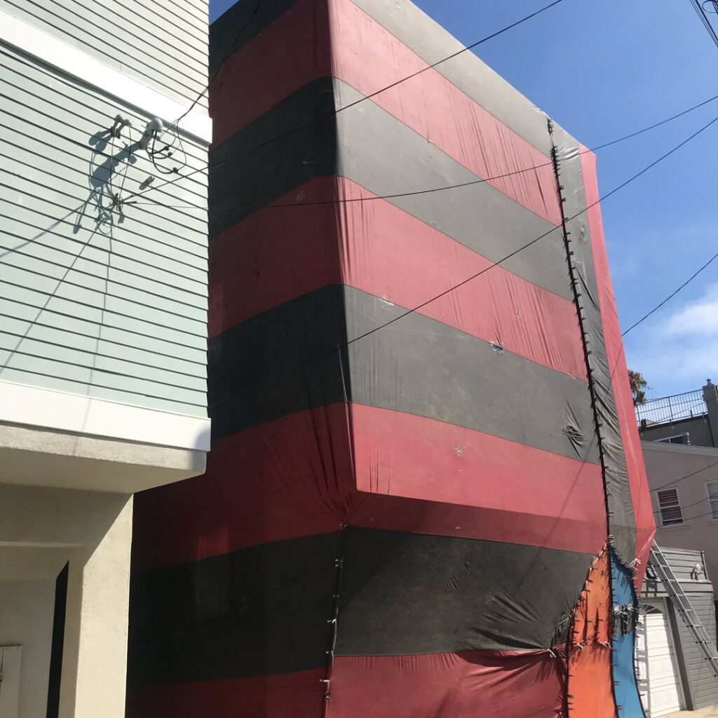 A section of a building covered in red and black fumigation tenting by Intensive Pest Control in Long Beach, CA.