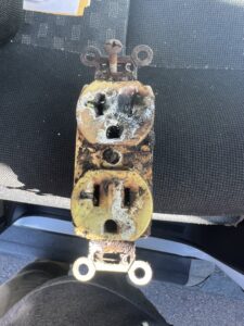 A severely burnt and damaged electrical outlet requiring repair from Myres Electrical Service in Mesa, AZ