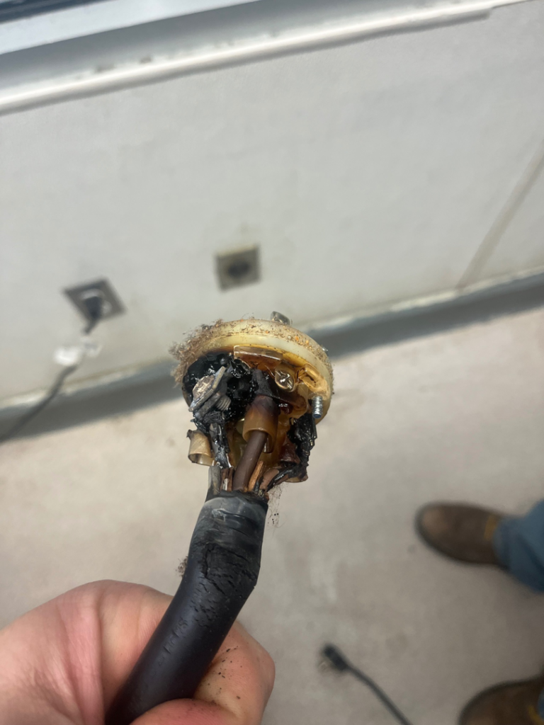 A severely burnt and damaged electrical plug and cord, indicating a fault, handled by ELEC LLC in Winston-Salem, NC.