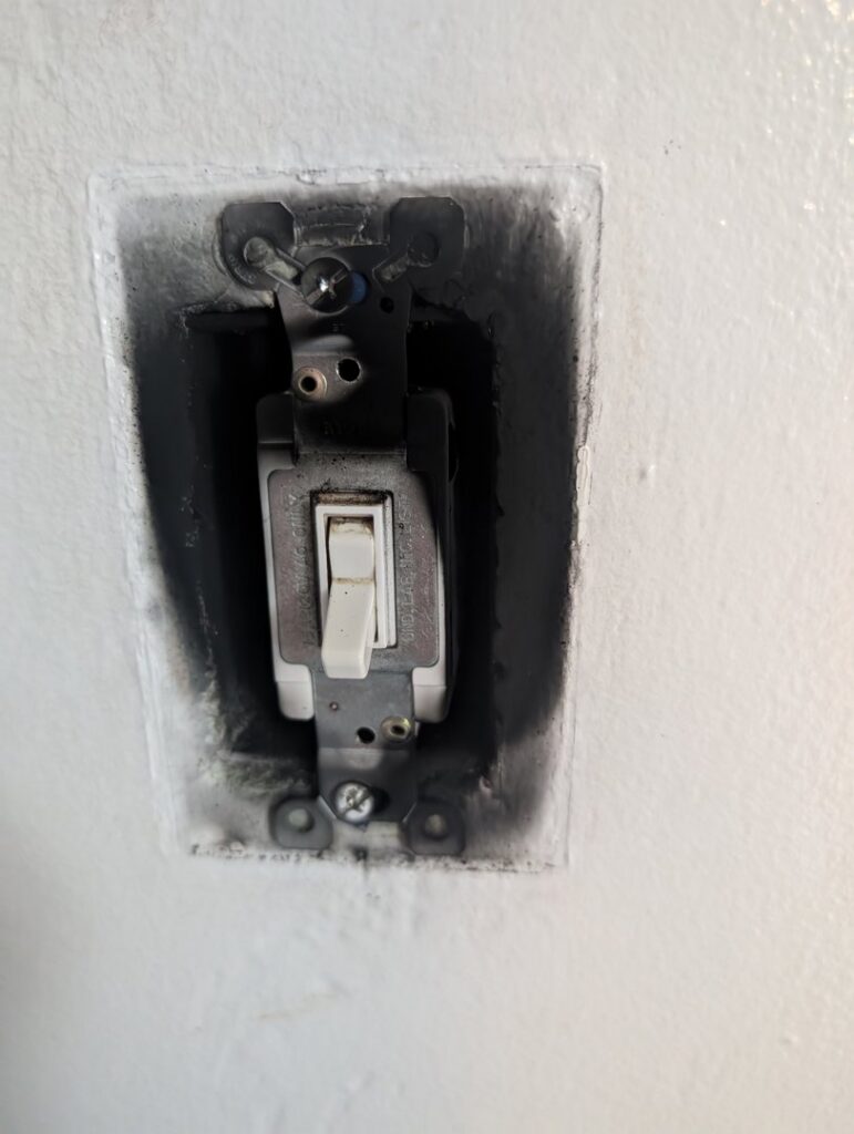 A close-up of a burnt or damaged electrical light switch, indicating a repair job by Maiolo Electric in Pittsburgh, PA.