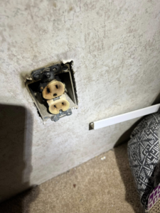 A burnt electrical outlet still in the wall, showing damage that KNK Electric in Pittsburgh, PA can repair.