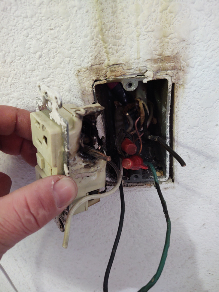 A close-up of a burnt and damaged electrical outlet being inspected for repair by BT Electric LLC in Gillette, WY.
