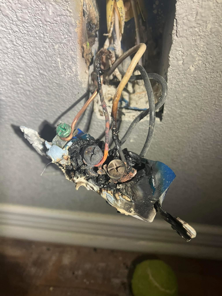 A severely burnt electrical outlet and wiring, indicating a repair job by AIM to Please Plumbing & Electric in Bloomington, IN.