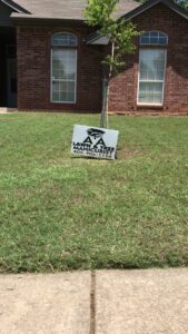 A 'AA Lawn & Tree Manicurist' business sign placed on a green lawn in front of a house by A & A Lawn Care Service LLC in Edmond, OK.