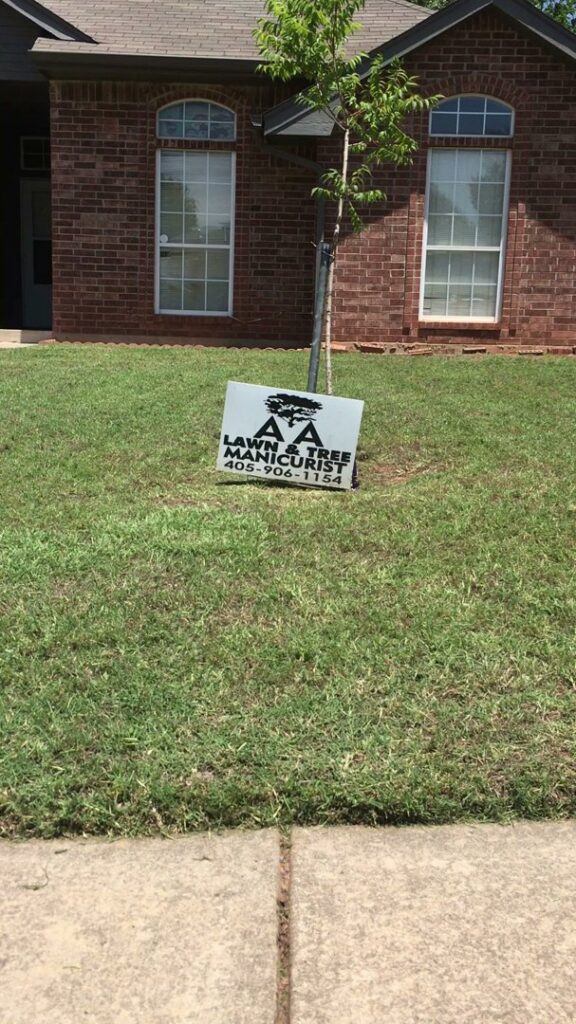 A 'AA Lawn & Tree Manicurist' business sign placed on a green lawn in front of a house by A & A Lawn Care Service LLC in Edmond, OK.