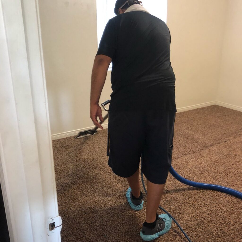 A carpet cleaning professional with a cleaning wand and hose, wearing shoe covers, performing a job for Alex's Janitorial and Carpet Cleaning in Bakersfield, CA