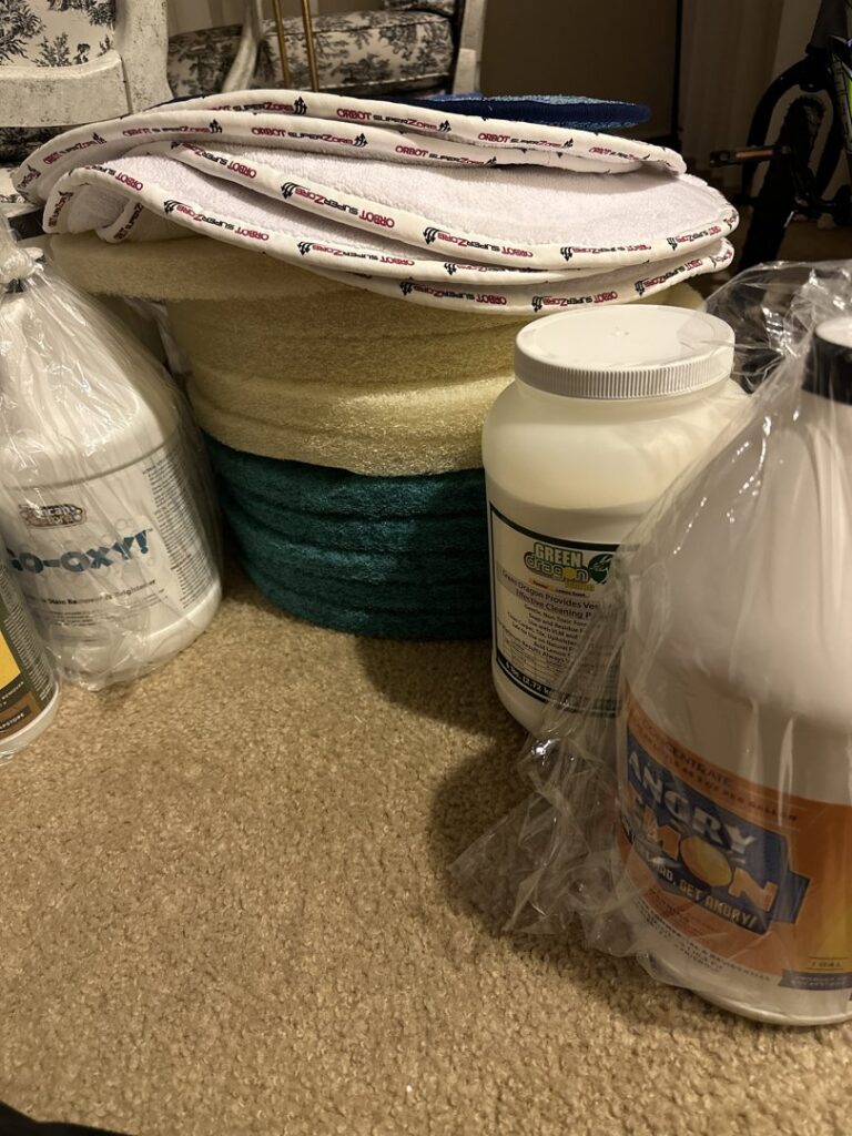 Carpet cleaning chemicals and stacked cleaning pads on a carpeted floor by Encapstore.com in Las Vegas, NV