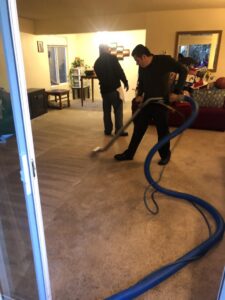 A carpet cleaning crew actively working in a living room, using professional equipment at Sunshine Carpet Cleaning Services in Houston, TX