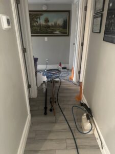 Carpet cleaning equipment, including hoses and a sprayer, set up in a hallway for a job by Extra Mile Floor Care in Mesa, AZ.