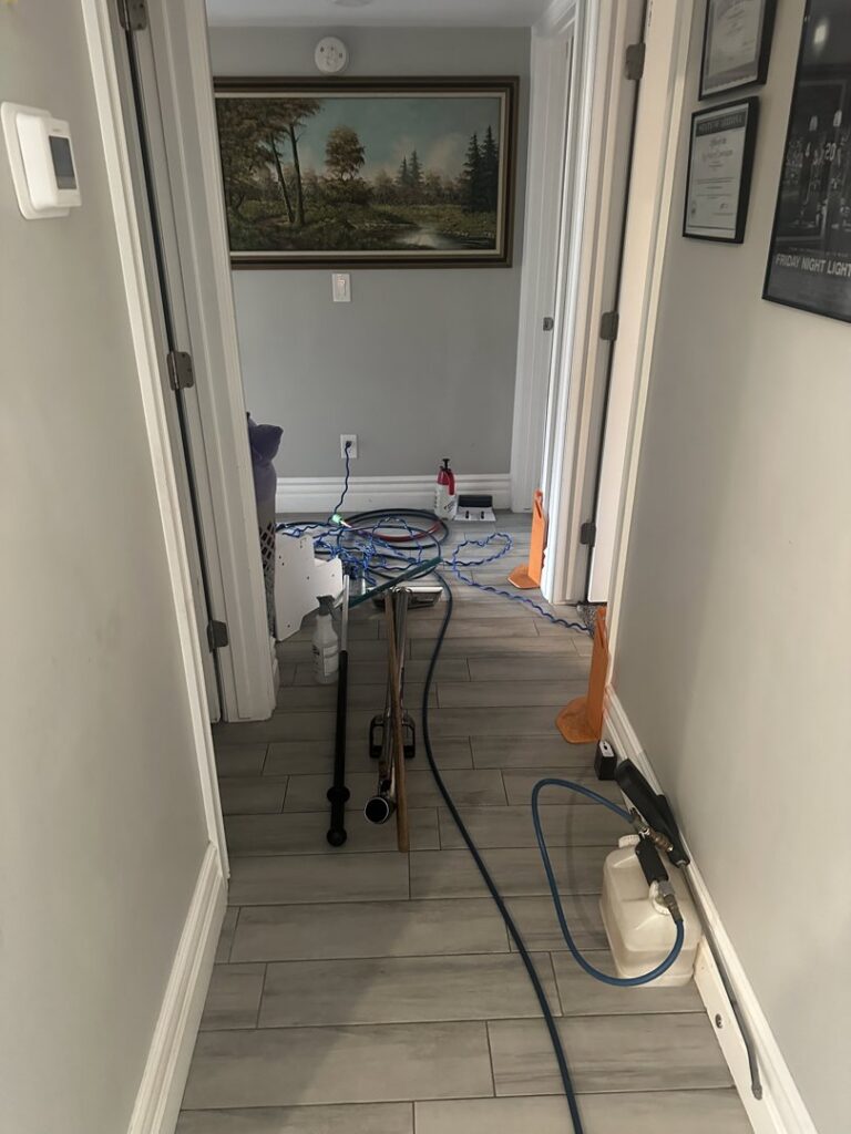 Carpet cleaning equipment, including hoses and a sprayer, set up in a hallway for a job by Extra Mile Floor Care in Mesa, AZ.