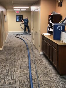 A worker setting up carpet cleaning equipment with hoses laid across a commercial hallway for Super Duper Carpet & Duct Cleaning in Pittsburgh, PA.