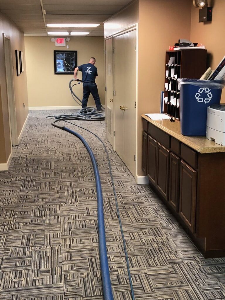 A worker setting up carpet cleaning equipment with hoses laid across a commercial hallway for Super Duper Carpet & Duct Cleaning in Pittsburgh, PA.