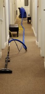 A carpeted hallway being professionally cleaned with a carpet cleaning wand and hoses by Genie Clean Services LLC in Dallas, TX.