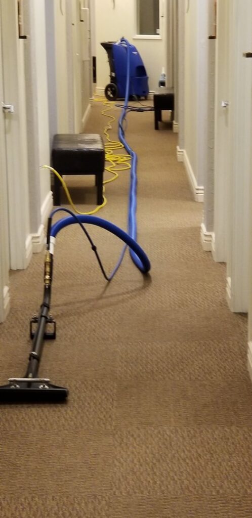 A carpeted hallway being professionally cleaned with a carpet cleaning wand and hoses by Genie Clean Services LLC in Dallas, TX.
