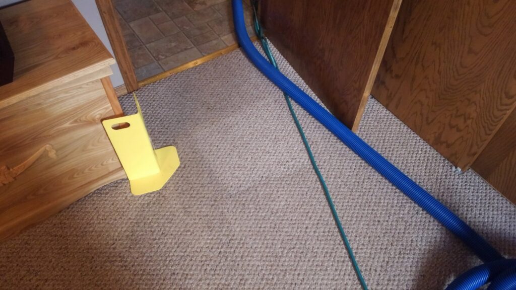 Carpet cleaning hose and a yellow door guard in a carpeted room by Customer First Carpet Cleaning in Appleton, WI