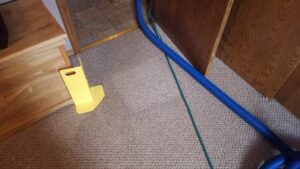 Carpet cleaning hose and a yellow door guard in a carpeted room by Customer First Carpet Cleaning in Appleton, WI