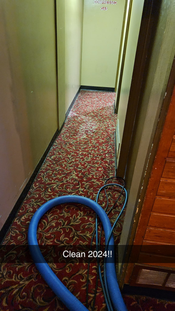 A blue carpet cleaning hose laid out on a red patterned hallway carpet during a job by Quality Carpet Cleaning in Lewiston, ID.