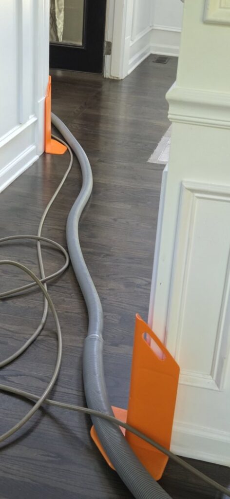 A carpet cleaning hose running across a hardwood floor with orange protective guards, indicating a professional cleaning setup by JDog Carpet Cleaning & Floor Care Alpharetta in Roswell, GA.