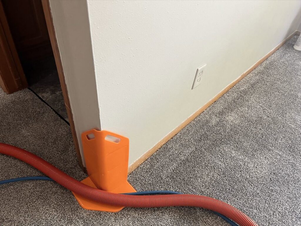 Carpet cleaning hoses with a corner protector on a carpeted floor, indicating work by Carpet Master in Aberdeen, SD.