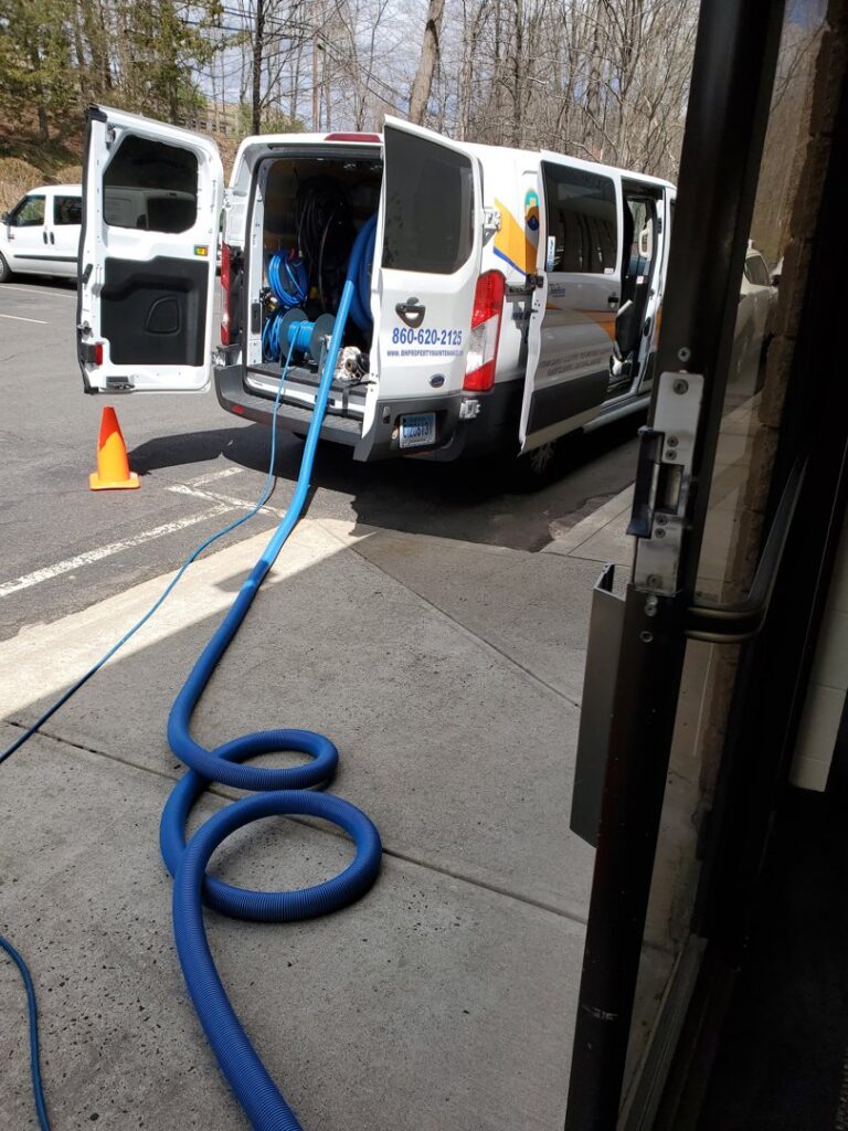 Long blue hoses extending from a B&H Property Maintenance LLC van for a carpet cleaning job in Middletown, CT.