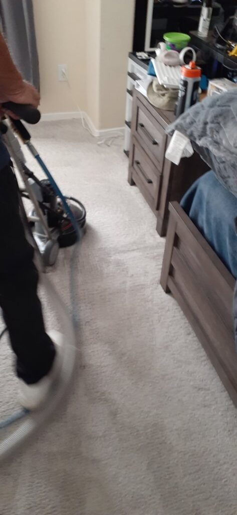 A professional operating a carpet cleaning machine on a light-colored carpet in a bedroom by El Paso Carpet Care in El Paso, TX.