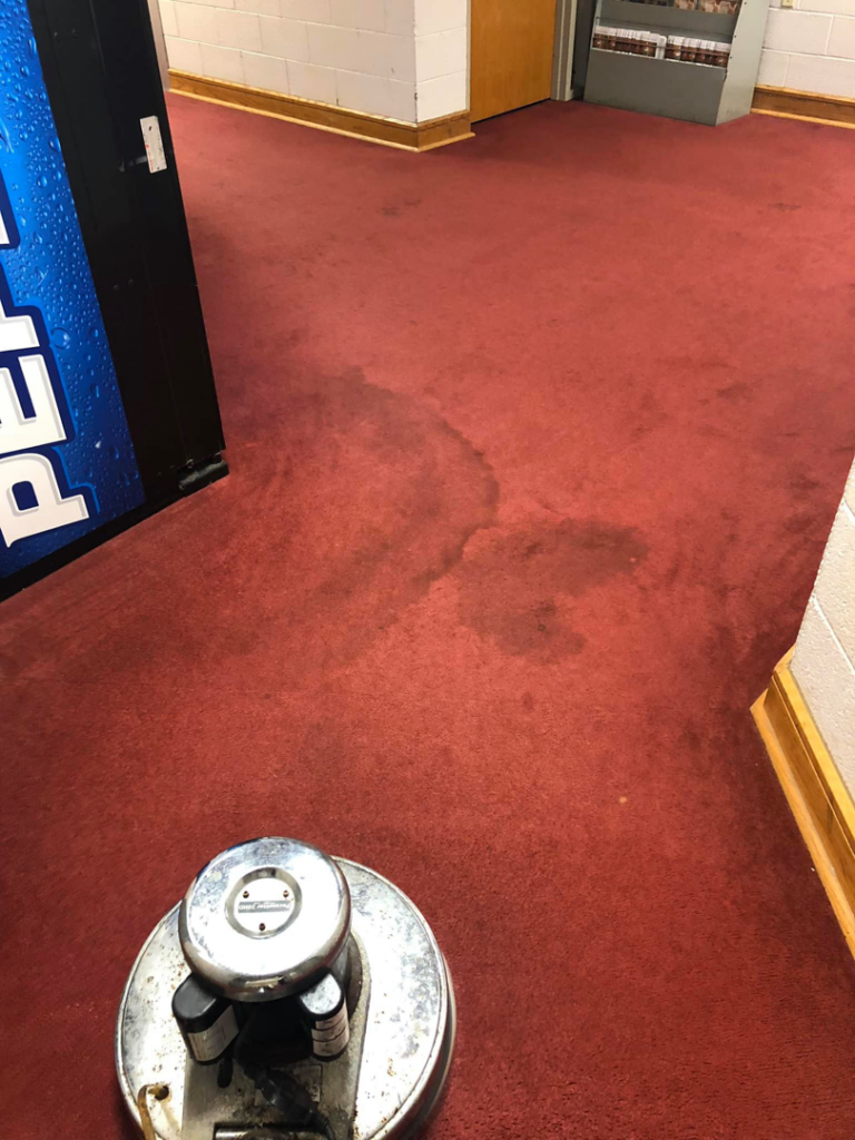 A professional floor cleaning machine actively cleaning a stained red carpet by Above and Beyond Cleaning Services, LLC in Aberdeen, MD