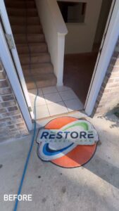 Carpet cleaning job setup at an entrance with a hose and branded mat by Restore Carpet Care and Tile in Tallahassee, FL