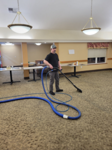 A professional from Interior Care Carpet Cleaning cleaning carpet in a large room with specialized equipment in Bend, OR.