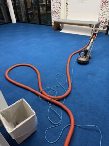 A carpet cleaning machine with hoses on a vibrant blue carpet, performing a job for Carpet Master in Aberdeen, SD.