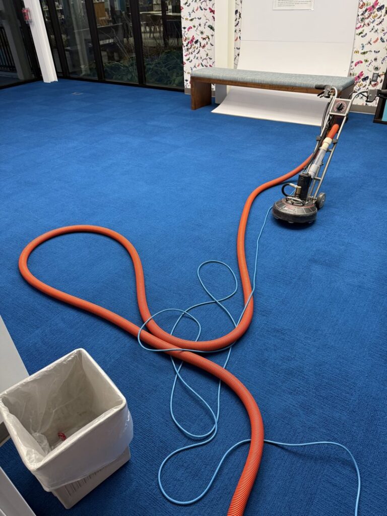 A carpet cleaning machine with hoses on a vibrant blue carpet, performing a job for Carpet Master in Aberdeen, SD.