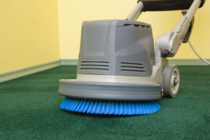 A professional carpet cleaning machine with a blue brush head cleaning a green carpet in Colorado Springs, CO by Rocky Mountain Dry Carpet Cleaning.