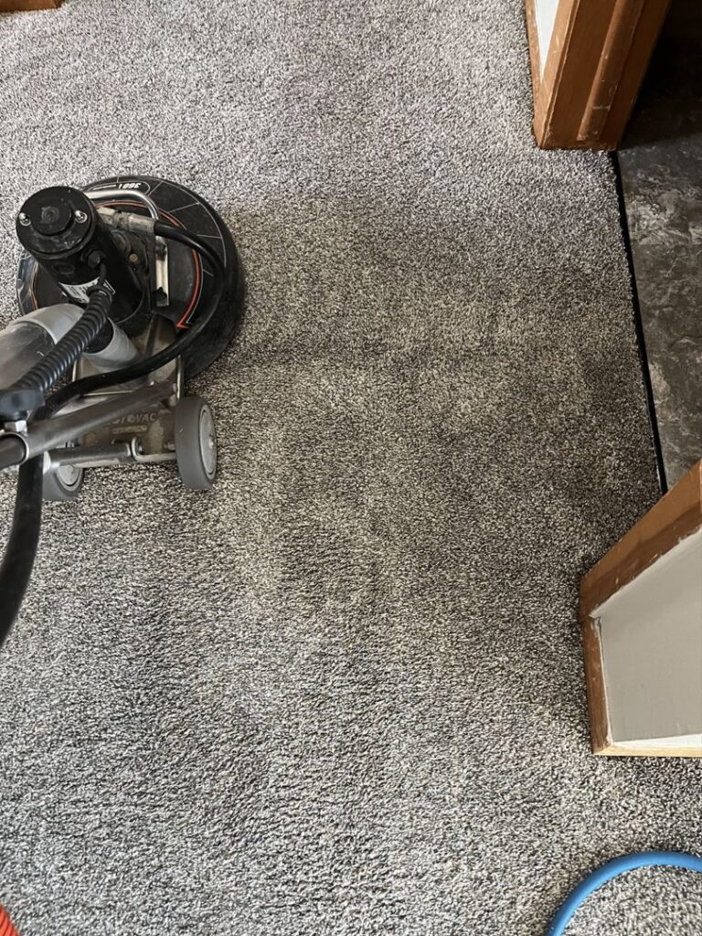 A carpet cleaning machine working on a grey carpet, showing the cleaned area by Carpet Master in Aberdeen, SD.