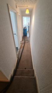 A carpet cleaning machine with hoses in a hallway during a job by Plymouth Carpet Cleaners in Hooe, UK.