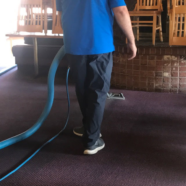A professional cleaning a purple carpet with a hose and wand for First Choice Janitorial Services in Vancouver, WA.