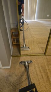 A carpet cleaning professional and their equipment reflected in a mirror while cleaning a carpet for KD Carpet Cleaning in Albuquerque, NM.