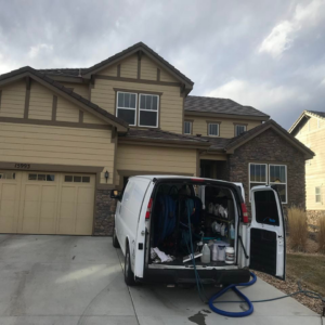 A Spot-On Carpet Care service van with open doors showing equipment parked in front of a house in Denver, CO.