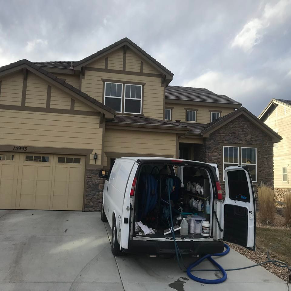 A Spot-On Carpet Care service van with open doors showing equipment parked in front of a house in Denver, CO.
