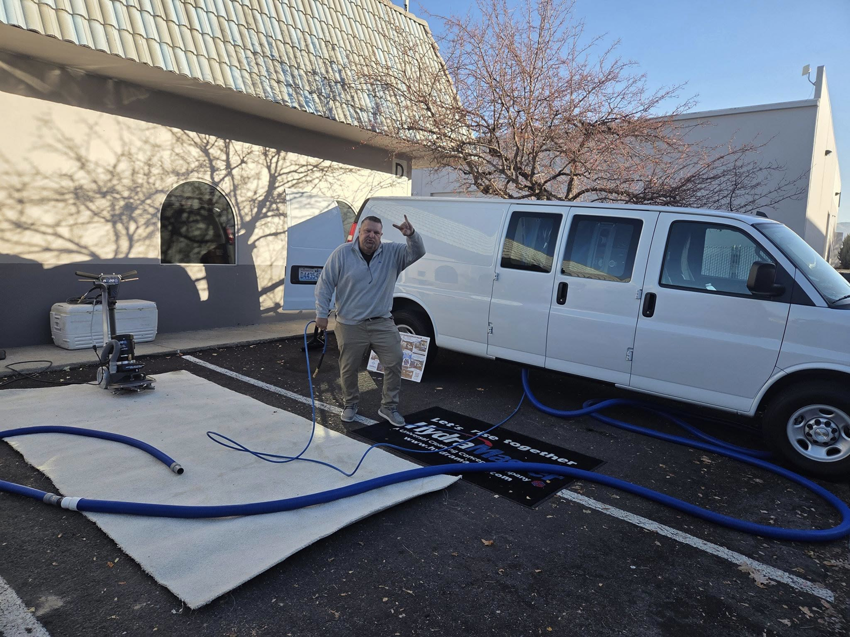 A man demonstrating a carpet cleaning setup with a van and equipment for Sierra Cleaning Systems in Sparks, NV.